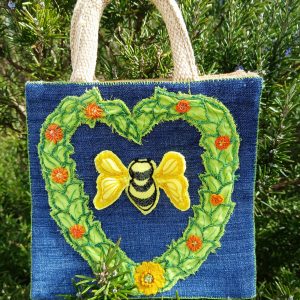 A photograph of a jute shopping bag embroidered with an image of a bumble bee in a heart of leaves and flowers