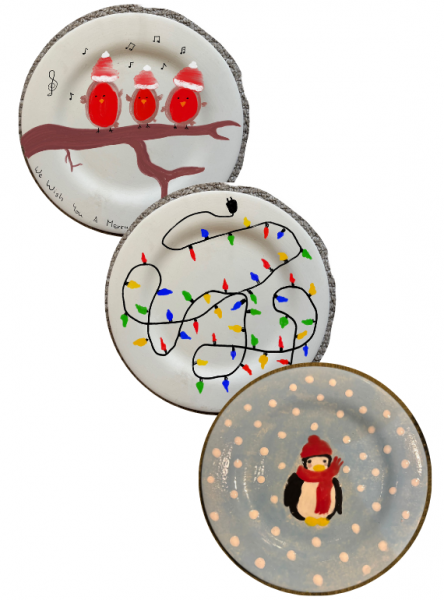 A photograph of three hand painted plates. One depicts three birds, in red costumes, singing on a branch, the second depicts a string of Christmas lights, the third is of a penguin wearing a red hat and scarf against a snowy background.