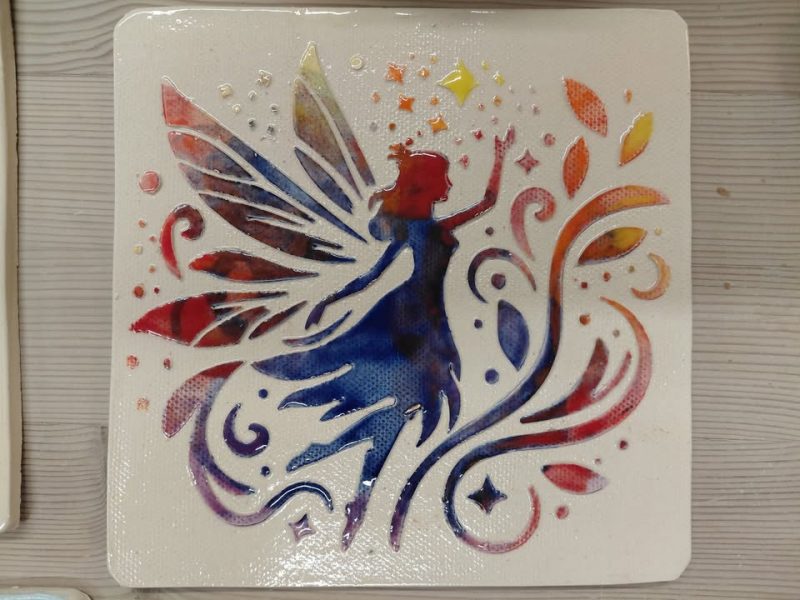 A photograph of a ceramic tile with a painted fairy