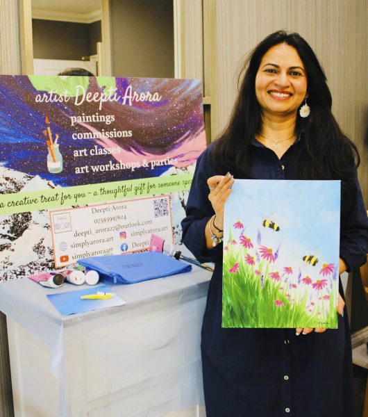 A photograph of the artist, Deepti Arora holding a bright painting